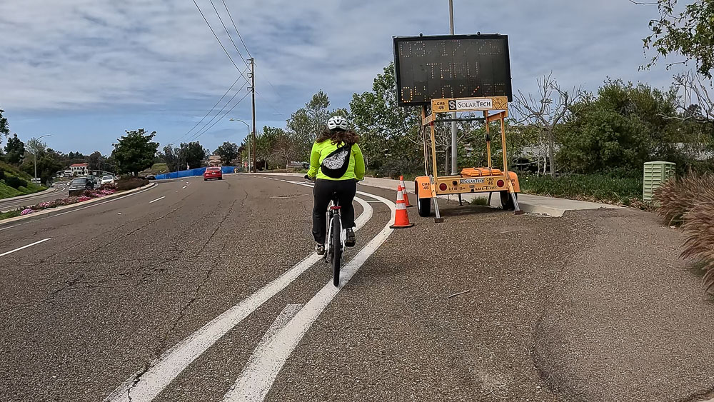 Cyclist passes a electronic construction sign that is positioned in the Class II bike lane on Encinitas Blvd. in Encinitas, California